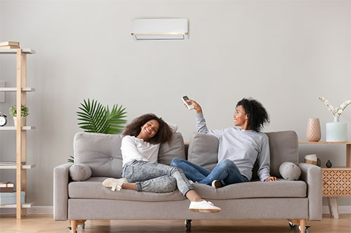 Two young women on sofa enjoying new air con installation from an ac company in Hertfordshire.